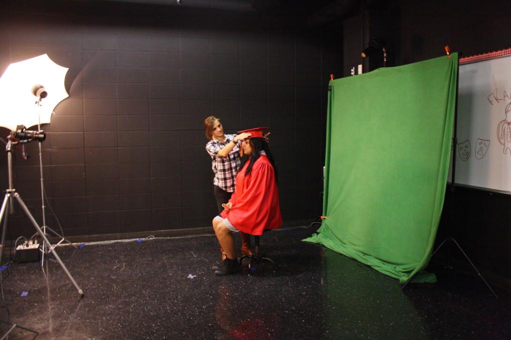 A photographer assists a student wearing the traditional graduation rope. 