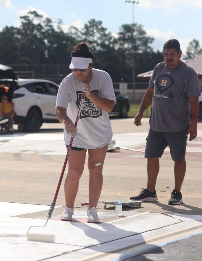 LET ME SEE. Senior Isabel Iracheta paints her parking spot white on Sept. 17-18 2022 while her dad, goes behind her to check on paint she has accidentally spilled earlier. Seniors were covering their parking sports a base color to cover previous designs or to start their own design.