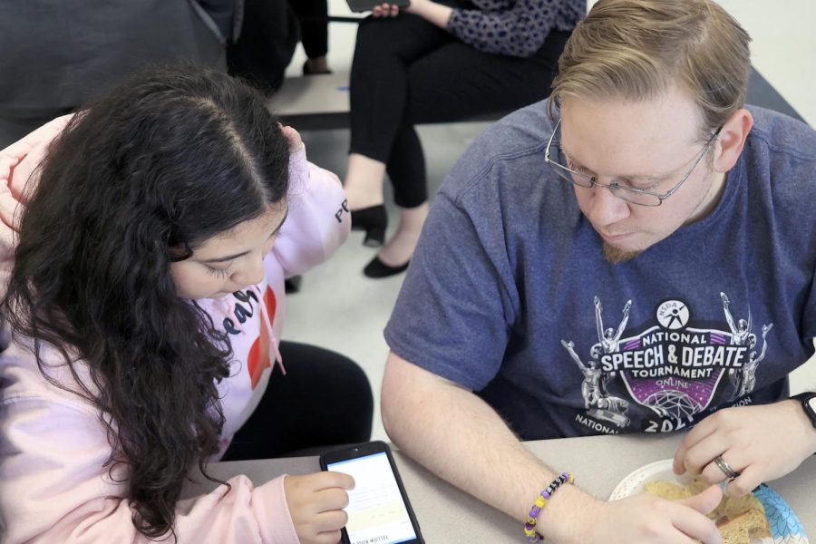 KEEPING TABS. Head coach Joseph Collatos shows sophomore Camila Blancas how to find her rounds and results on Tabroom.com on the first day of the Yellow Rose District national tournament qualifier at West Hardin High School on Wednesday, Feb. 15 Tabroom.com is where all official rounds, judges and results are posted for contestants to find their rooms. Students often have to find rooms and keep up with their own schedules while the coaches are judging other rounds.