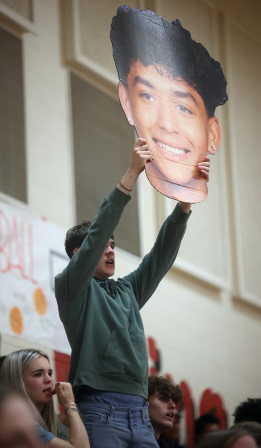 BIGGER IS BETTER. Sophomore Hayden Herrington holds up a huge cut out of Senior Ethan Lozano on Jan. 18, 2023. The cut out is held at the boys basketball game by other students as well.

