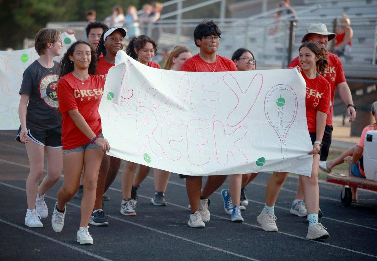 WALKING PROUD. Senior Mary Ruelas holds up a Tennis poster with a fellow teammate as she walks down the track field for the homecoming parade on Wednesday, Sept. 13. Tennis was one of the many sports that participated in the parade to showcase spirit for homecoming. “It was a fun experience because I’ve never been to a homecoming parade before,” Ruelas said. “It was a nice bonding time with my teammates.”