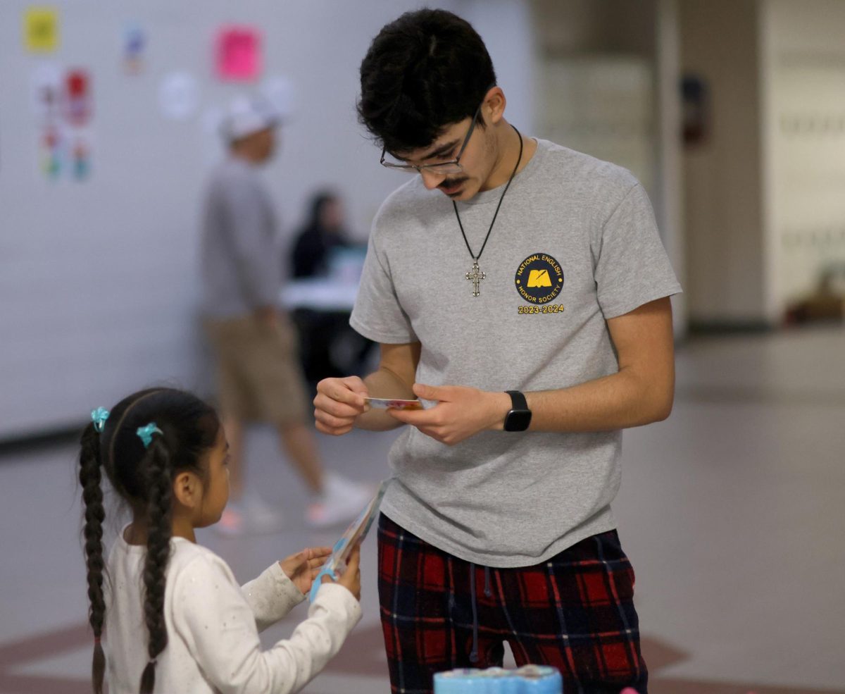 Senior Humberto Saenz helps a child pick out a card from the prize table on Saturday, March 2, 2024. The Story Night Event was sponsored and organized by English teacher, Zachary Taylor and Special Ed teacher Katie McDevitt. 
