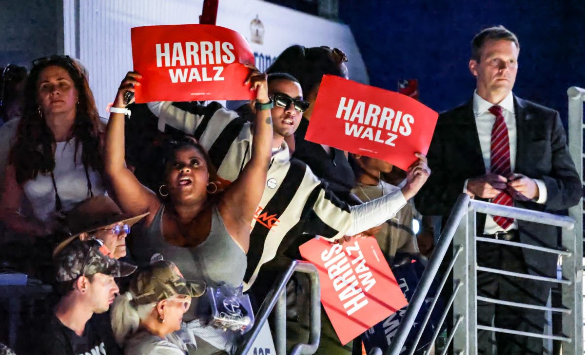 HANGING OFF. Kamala Harris Supporters in the stands of the NRG Stadium hold Harris Walz signs while leaning over the railing at the top floor on Oct. 25 at the Houston Rally. The rally held up about 30,000 viewers, filling the seats around the stadium.