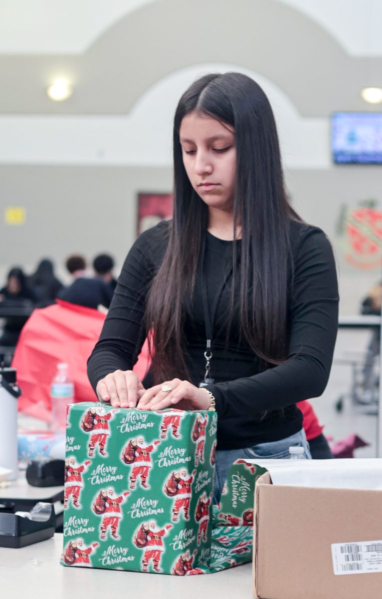 WRAPPING. Sophomore Abigail Murrillo leans over the table; putting the last tape on a present for a student at the winter thrift store held by STUCO on Dec. 12.