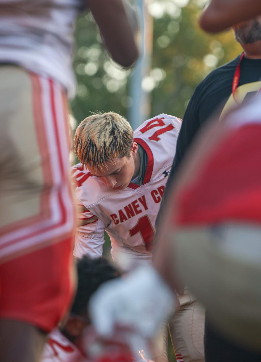 HALFTIME HUDDLE. Freshman Deacon Perry stands in the huddle during half time at the game on Aug. 4, 2025.Perry reaches down to grab his helmet during half time while listening to his coach. “ I think we weren’t prepared for the game.” Perry said. “I think we have great potential for the season,” Perry said.