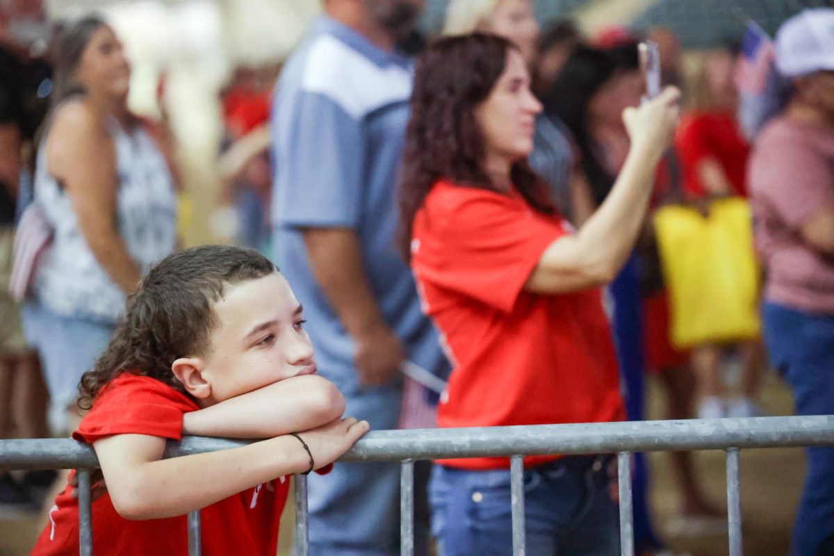 HERE FOR MOM. A child audience member rests his head on the sanctions in front of the stage of the Montgomery Fairgrounds stadium during the Charlie Kirk Memorial Service Sept. 30. In the background of the photo is the child’s mother taking photos of Judge Wayne Mack on stage.