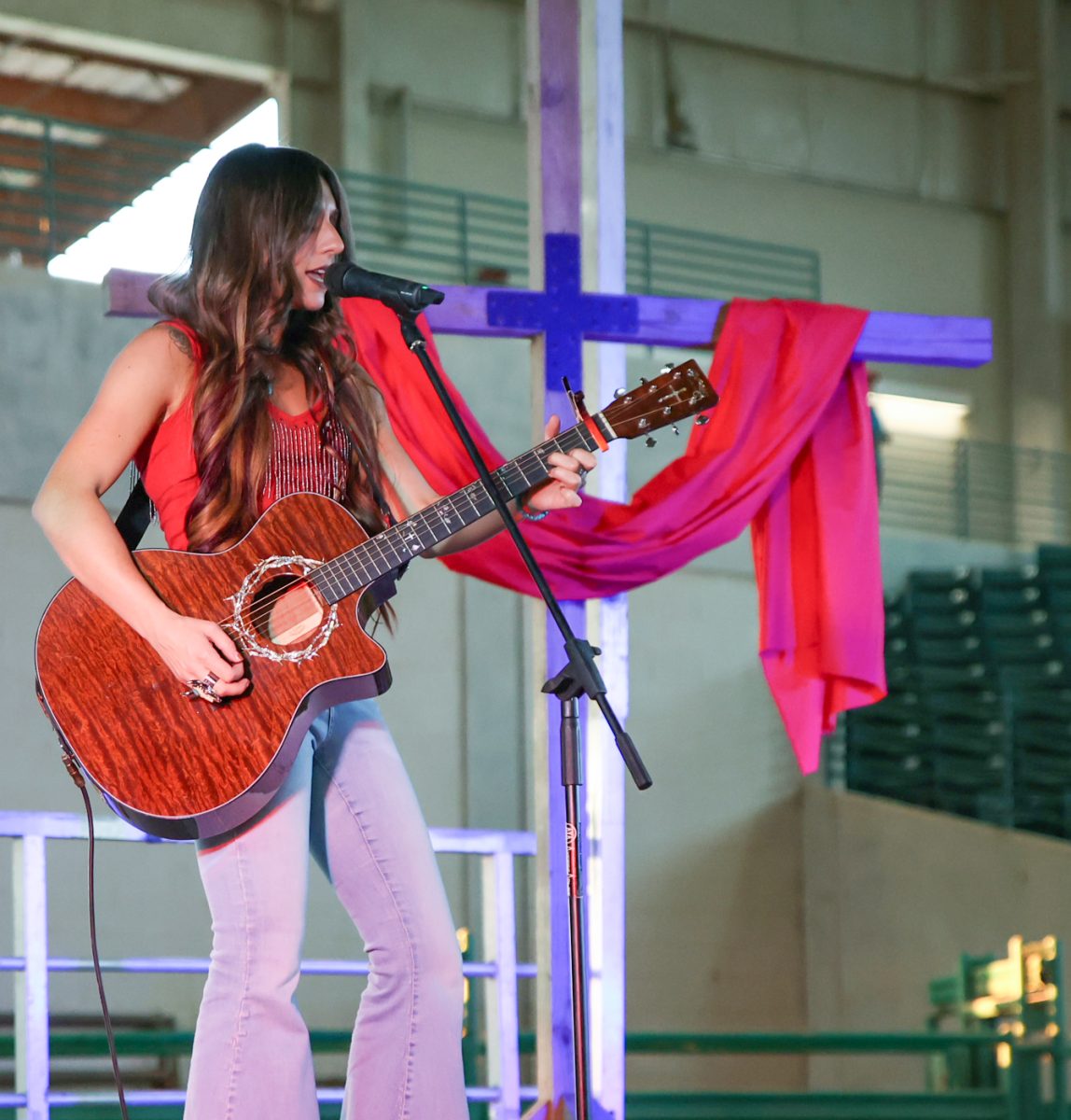CHORDS TIE TOGETHER. Country singer Payton Howie plays acoustic guitar in front of a cross on stage during the Charlie Kirk memorial service at the Montgomery Fairgrounds Sept. 30. During her performance, audience members raised their hands in worship.