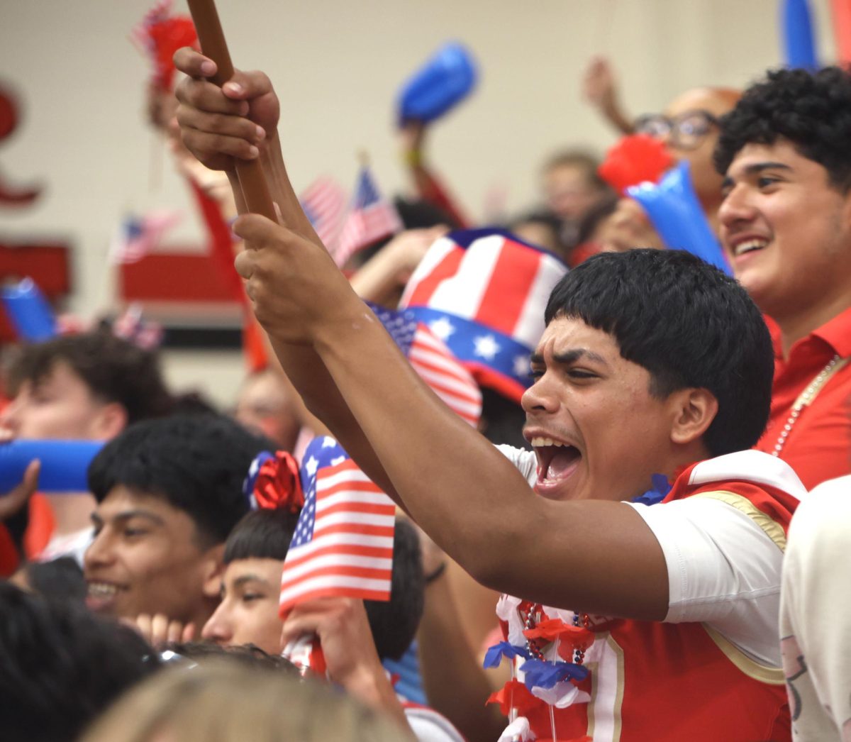 SPIRIT BANNER. Junior Kristopher Gordillo waves the American flag on the junior side during the pep rally on Sept. 12, 2025. The junior side was trying everything they could, trying to beat the seniors that were across the gym.