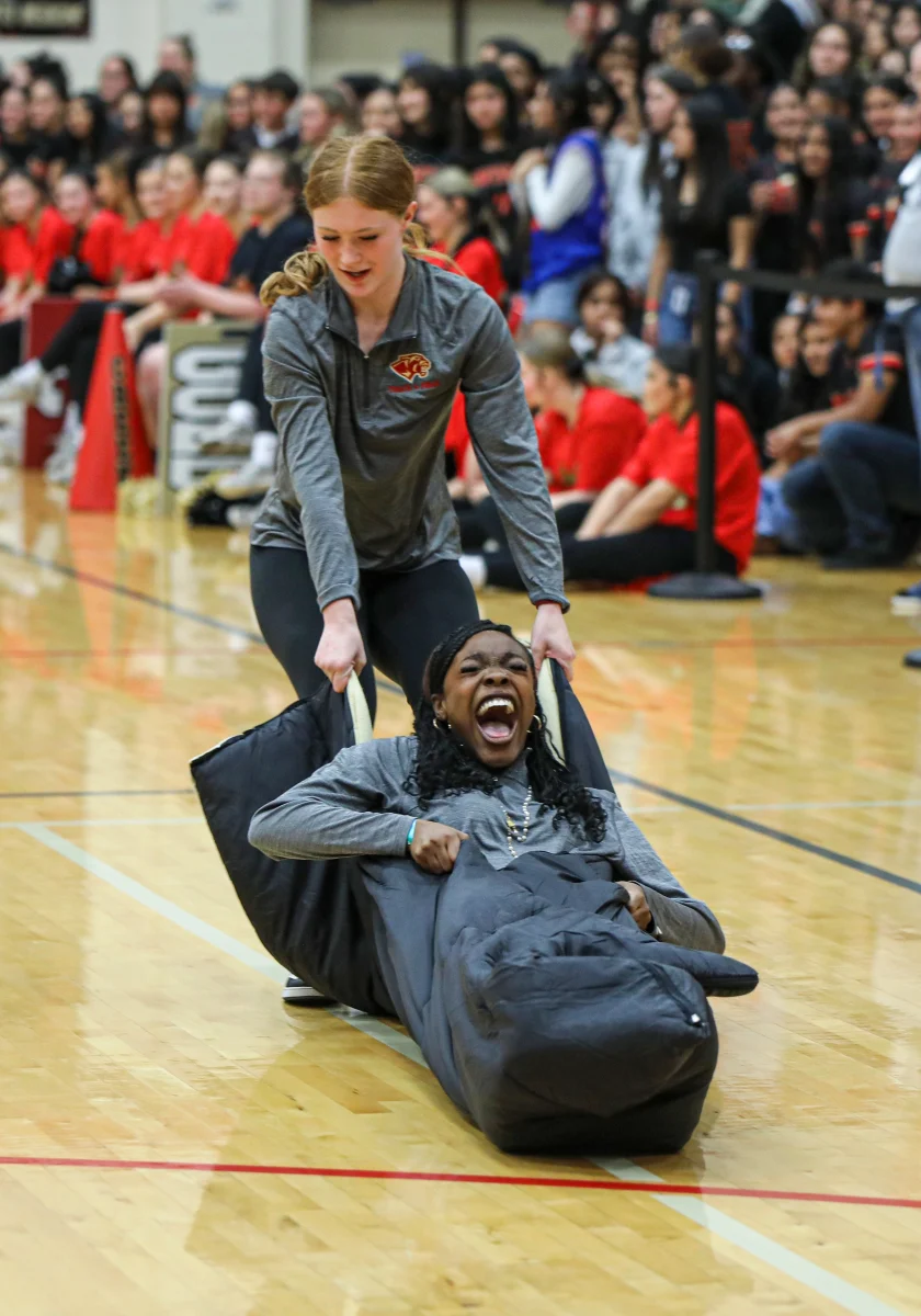 GAME ON. Freshman Kaydance Wood drags junior Diamond Picou by pulling her in a sleeping bag against the gym floor during the winter sports pep rally on Feb. 5, 2026. Both girls and boys track teams were competing against each other by racing back and forth across the gym while pulling another person from the track team.