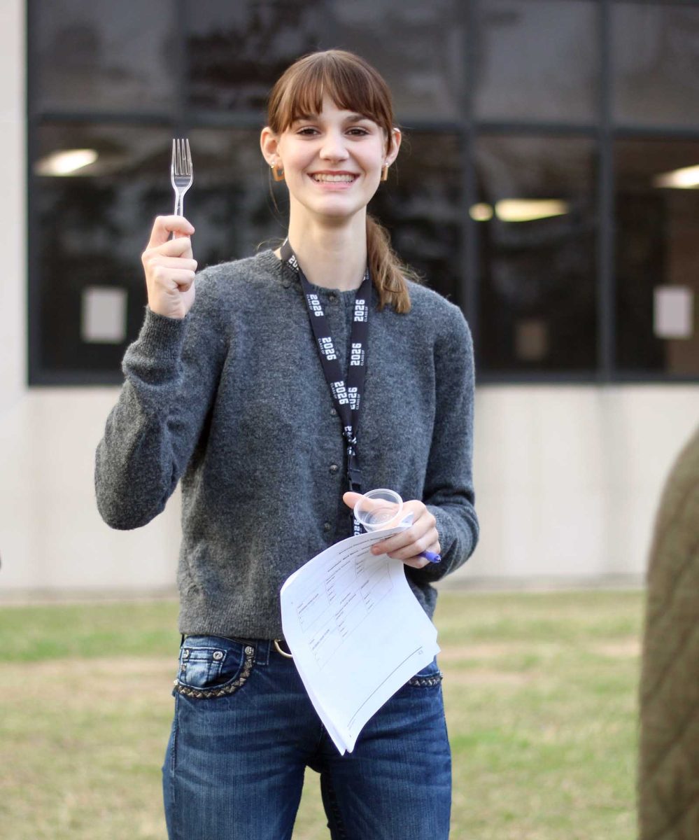 FORKED Senior Riley Blanks stands outside holding the fork she used for the AP Biology lab held on Thursday, Feb. 19, while laughing with her classmates. Students each had different utensils to pick from to conduct their bean experiment. “I had fun doing it because most labs we usually stay inside but we got to go outside and dig in the dirt,” Blanks said. 