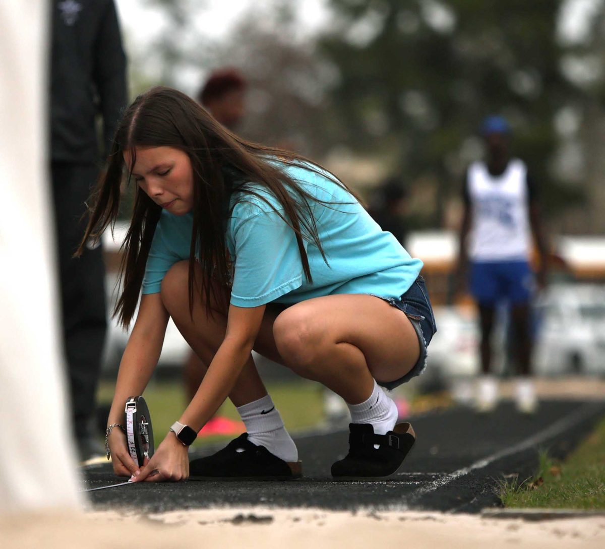 MEASUREMENT MANAGER. Junior Stella Domenget measures how far the past opponent jumped in the long jumps part of the Panther Relay Track meet on Thursday, Feb. 26, 2026. With Domenget getting volunteer hours for the National English Honor Society, she was put to measure the distance of long jumps. “I thought it was cool,” Domenget said. “I've never watched long jumps before so I was just watching them and seeing how far they could jump.”