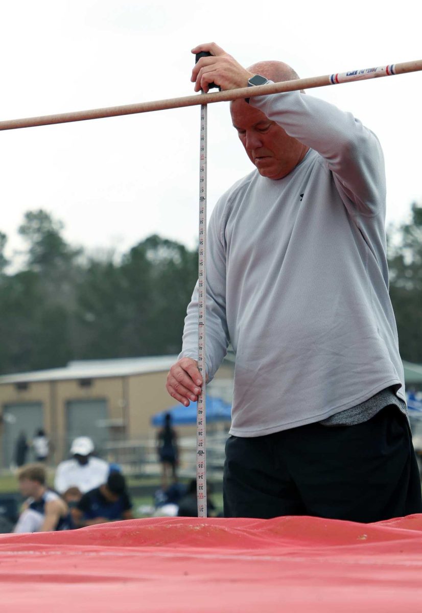 DON'T TOUCH IT. Track Coach Shawn Halloran preps the pole for a high jump before letting the competitor start their round during the Panther Relay Track meet on Thursday, Feb 26. Poles are measured before a high jump to ensure fairness between competitors.